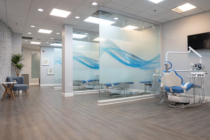 A modern dental operatory with a glass partition, a dental chair and an overhead light, of the kind Dr. Arpan Patel works in.